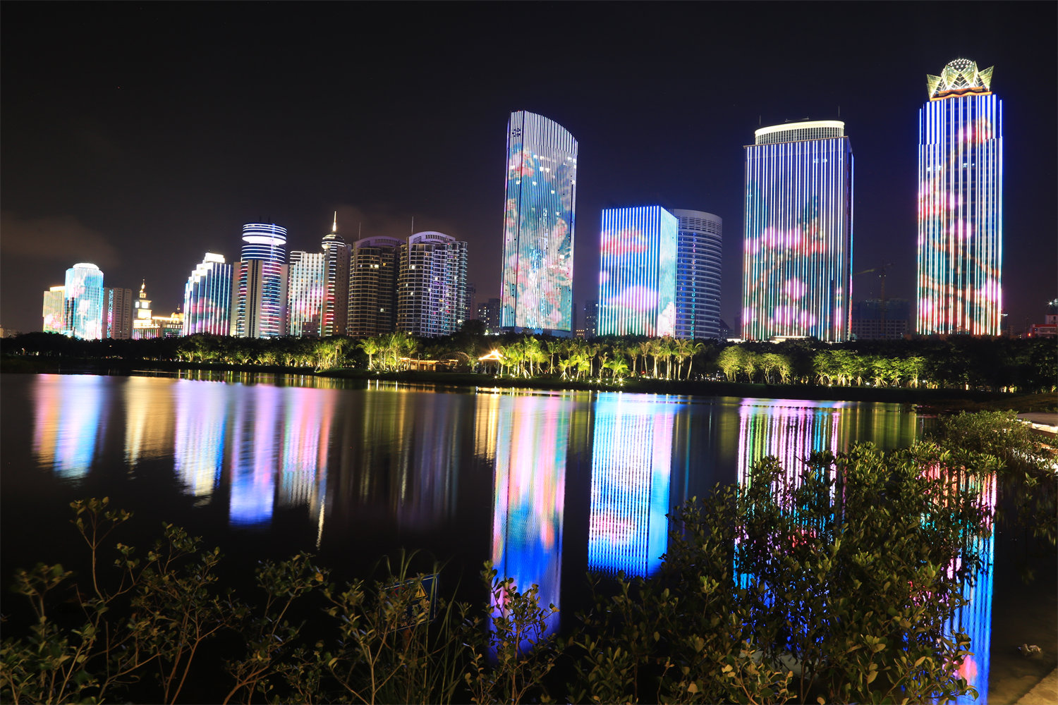 夜幕降臨，海口濱海大道高樓大廈的夜景為白日里休閑愜意的萬綠園增加一點時尚氣息。