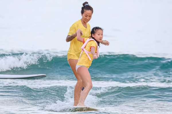 青少年兒童在沖浪教練的陪同下，在三亞市海棠區(qū)夏日水上運動嘉年華灣“乘風破浪”。三亞市體育旅游協(xié)會供圖